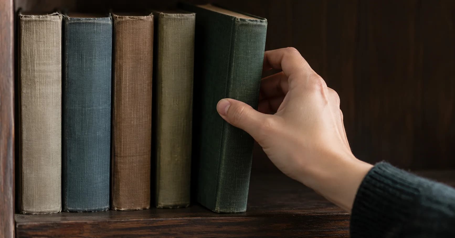 Una mano retira un libro de una pequeña fila de volúmenes encuadernados.
