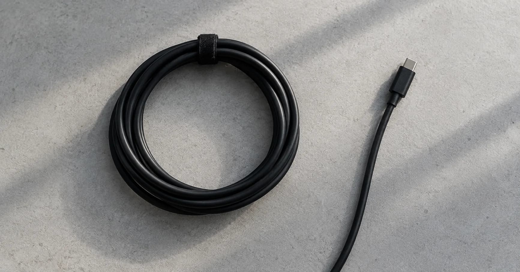 Un cable negro ordenado sobre una superficie gris con luz lateral.