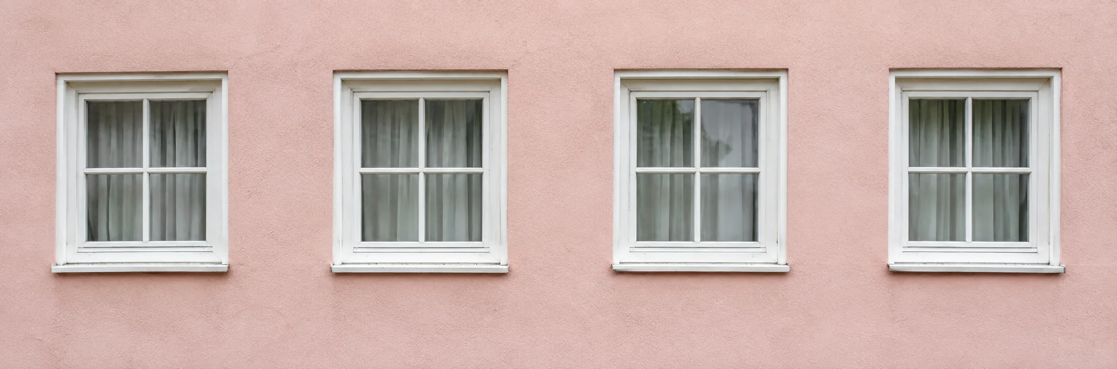 Ventanas de marcos blancos ordenan una fachada rosada.