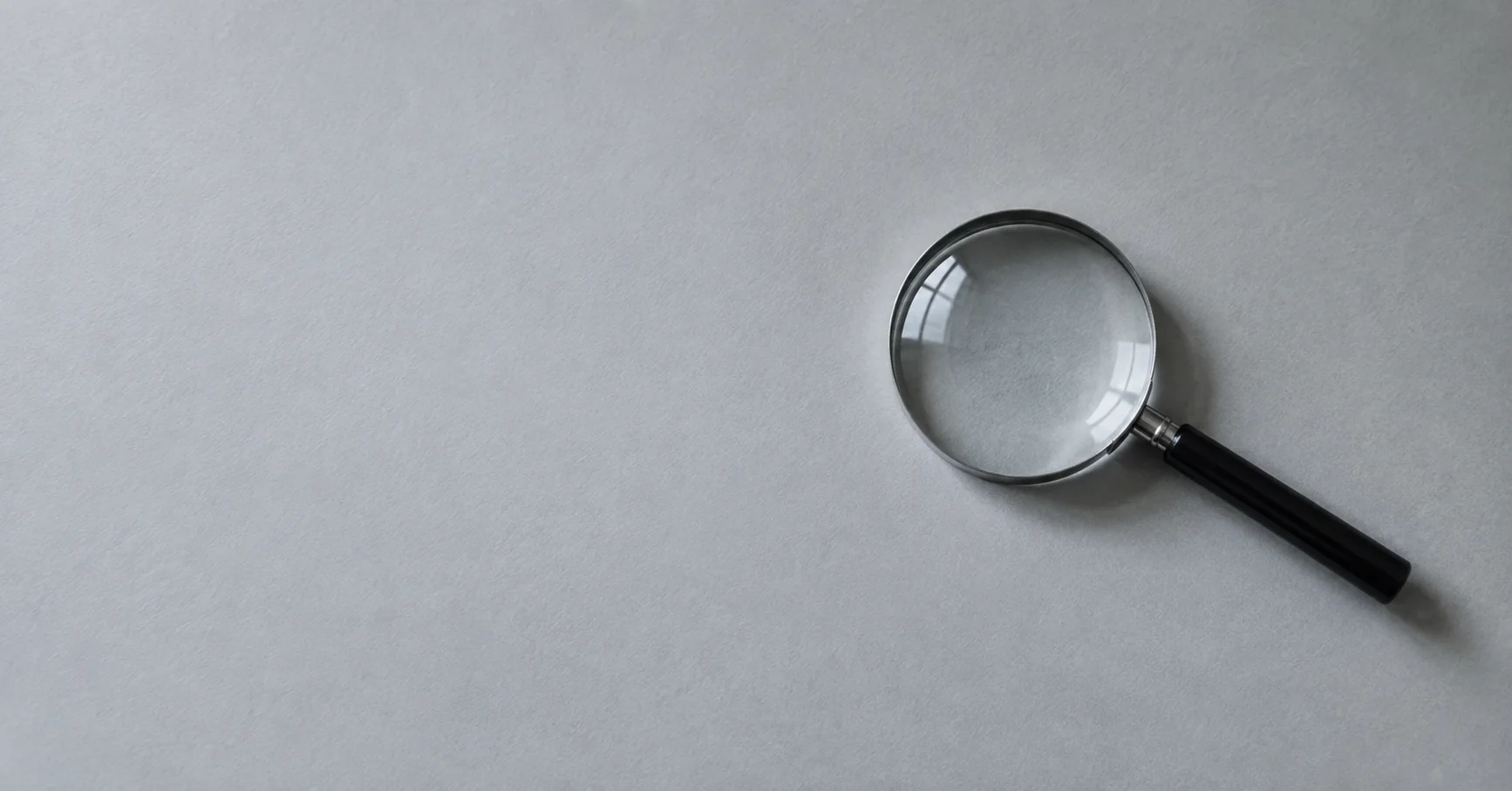 Una lupa sobre papel gris refleja suavemente la luz de una ventana.