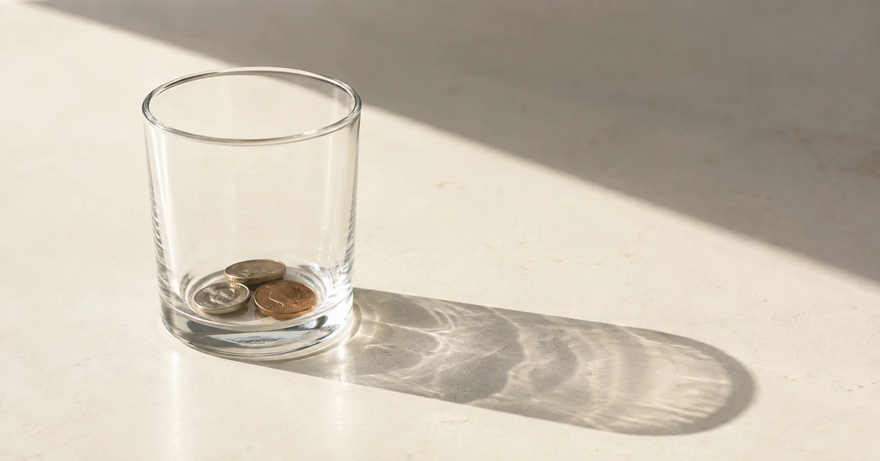 Unas monedas dentro de un vaso transparente proyectan una sombra sobre la mesa.