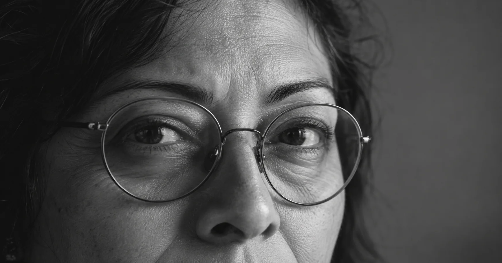Detalle en blanco y negro de una mirada atenta detrás de unos anteojos.